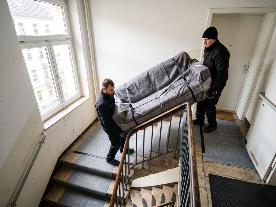 Zwei Umzugshelfer tragen ein verpacktes Sofa über ein Treppenhaus nach unten